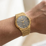 Wrist worn of Gold-tone stainless steel watch with grey textured dial, date display, and integrated bracelet