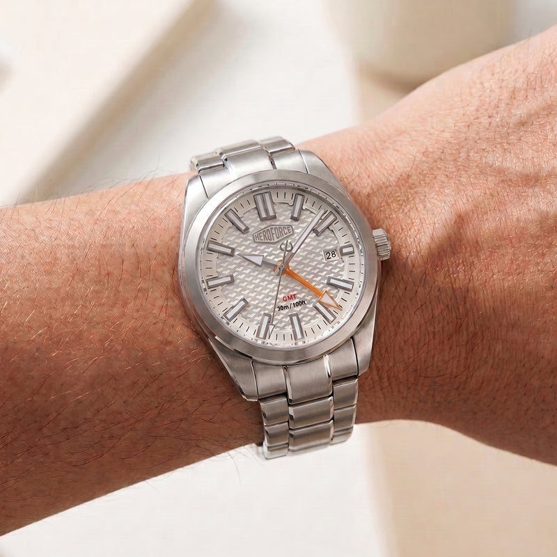 A silver stainless steel wristwatch with a textured white dial and orange hands, shown worn on a person's wrist.