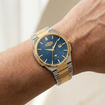 A two-tone wristwatch with a blue sunburst dial and gold and silver metal bracelet, shown worn on a person's wrist.