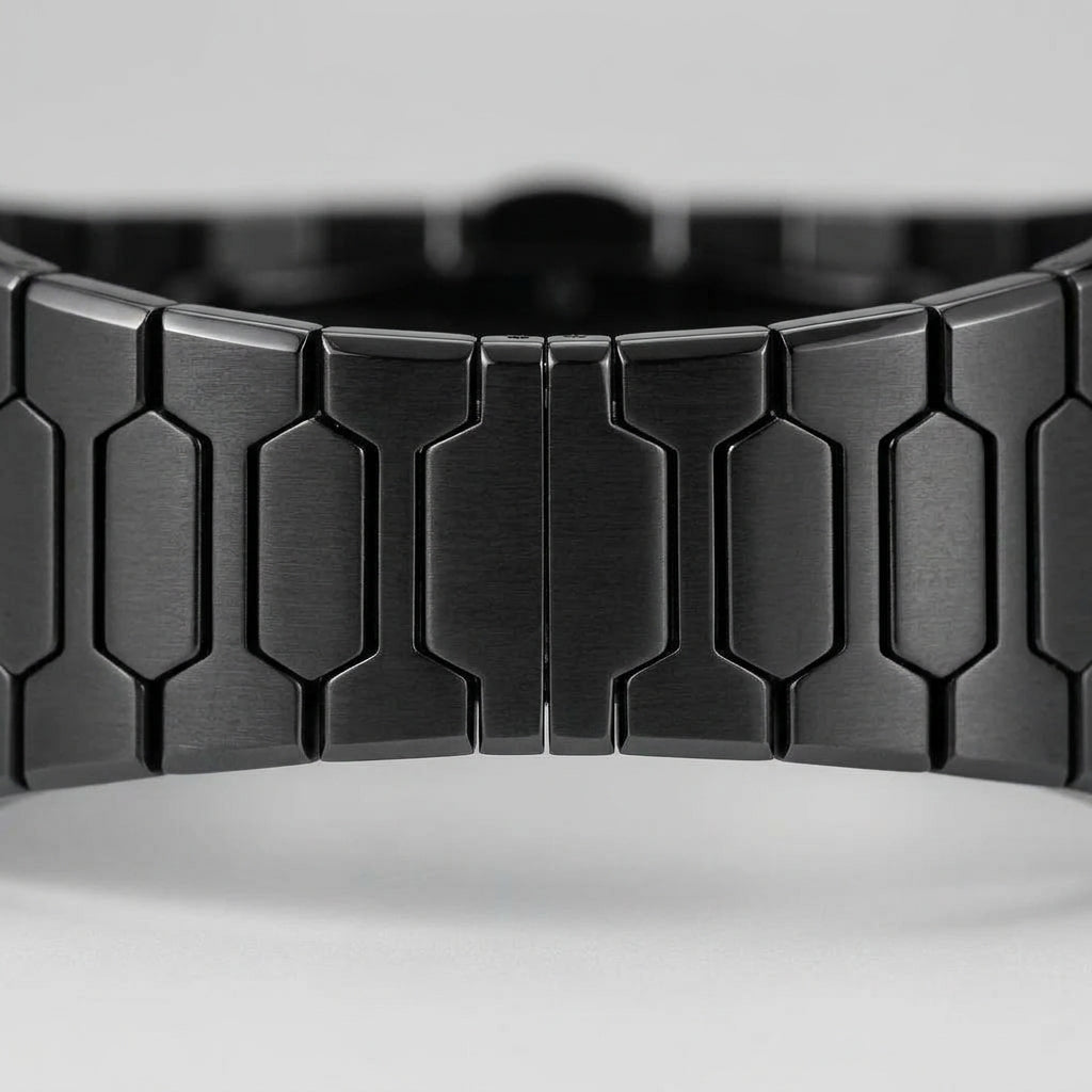 Close-up of a black metallic link watch band with a brushed finish and geometric hexagonal links, shown against a light gray background.