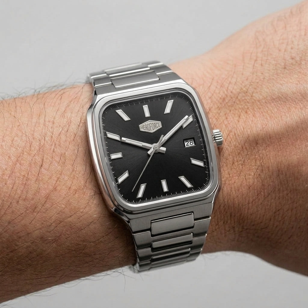 A silver-toned metal wristwatch with a black dial and rectangular cushion-shaped case, shown worn on a person's wrist