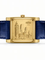 A square gold-tone wristwatch with a blue leather strap, shown from the back.