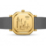 A gold-toned wristwatch shown from the back, featuring an engraved London cityscape on the case and a dark gray textured strap, photographed on a clean white background.