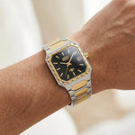 A two-tone stainless steel and gold watch with a black dial, shown worn on a person's wrist.