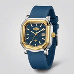 A men's analog watch with an octagonal bezel, featuring a blue textured dial, gold-tone hands and markers, a silver-tone case, and a blue silicone strap, shown on a light gray background.