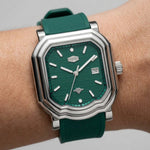 A close-up of a wristwatch with a green textured dial and matching green strap, worn on a person's wrist.