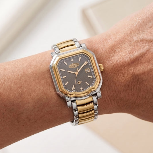 A two-tone wristwatch with a gold and silver link bracelet and a dark gray dial, shown worn on a person's wrist.