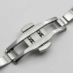 Close-up of a polished stainless steel watch band clasp on a light gray background.